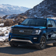 A photo of a blue Ford Expedition SUV driving on a snowy path.